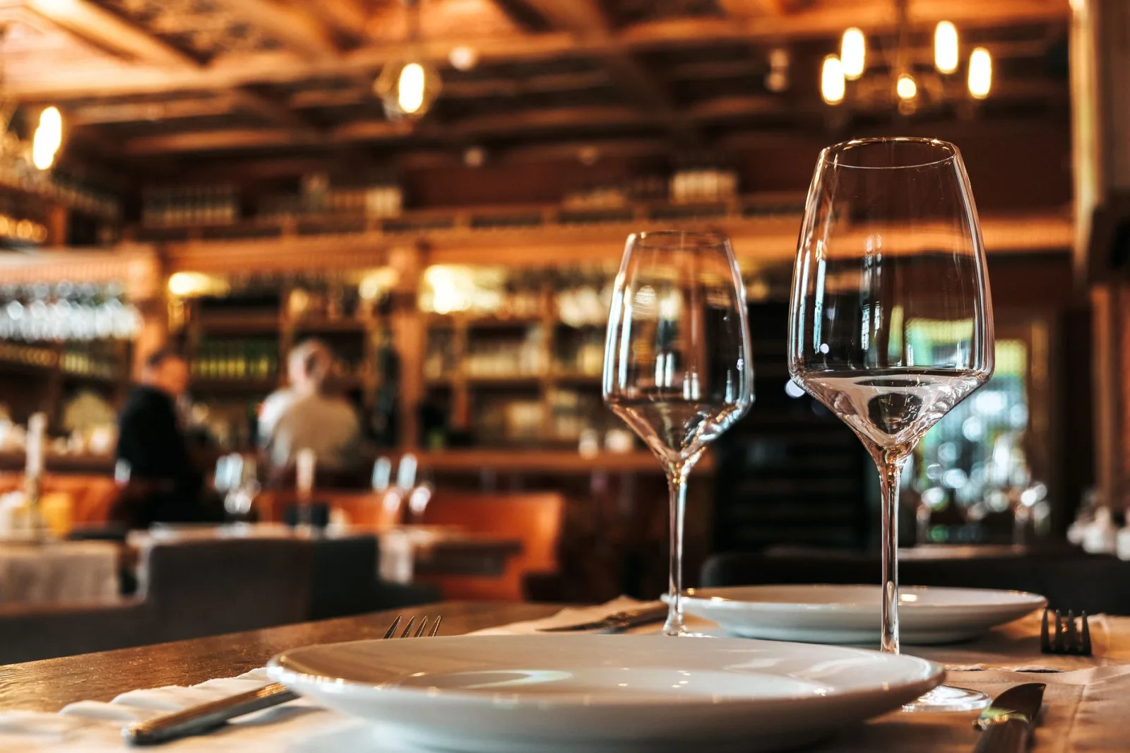 Elegantly set dining table with glassware in a cozy, warmly-lit restaurant ambiance.