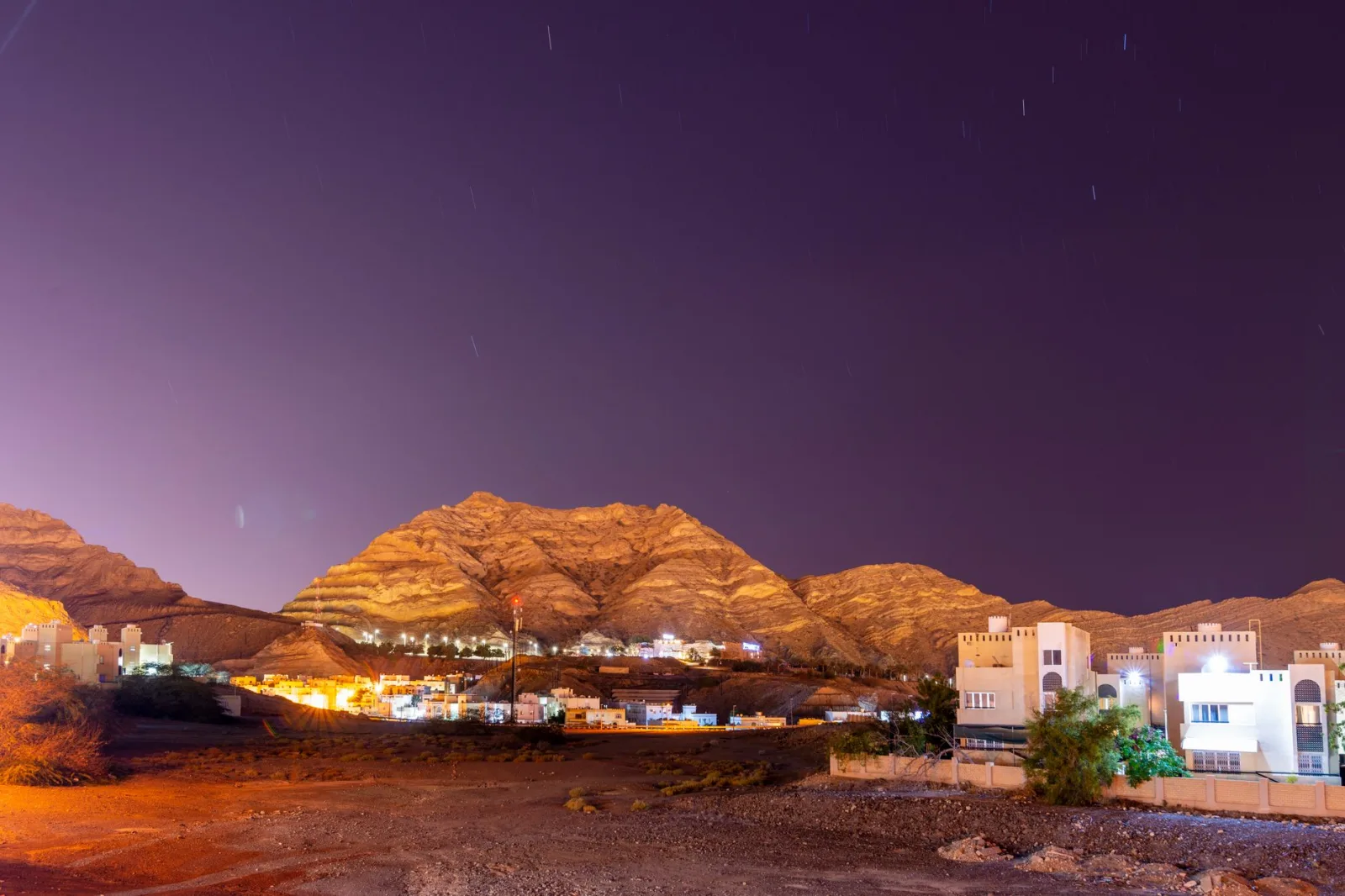 Scenic night landscape of a town in Oman with illuminated buildings against mountains.