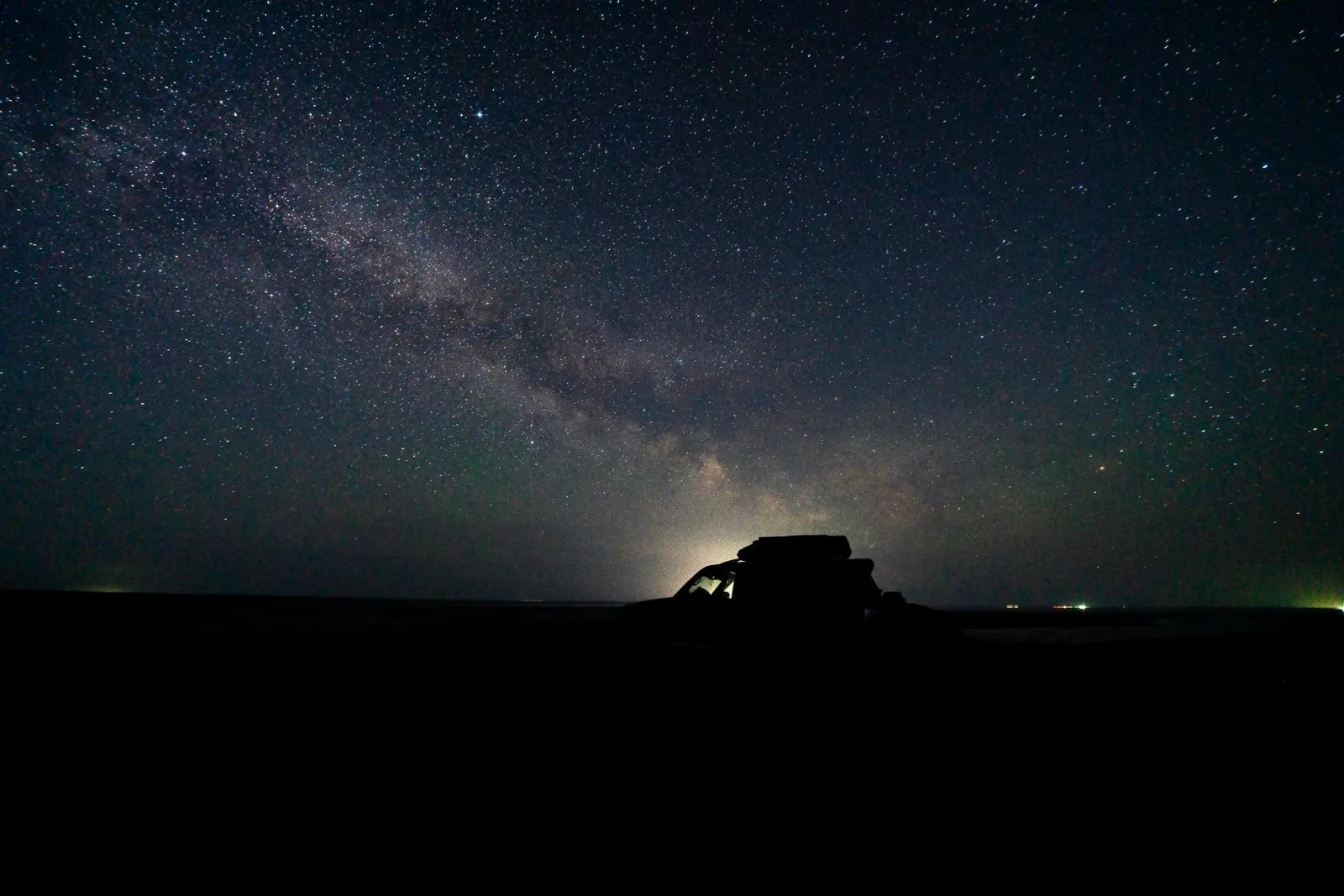 A stunning night view of a silhouetted car beneath the breathtaking Milky Way, showcasing the vast starry sky.