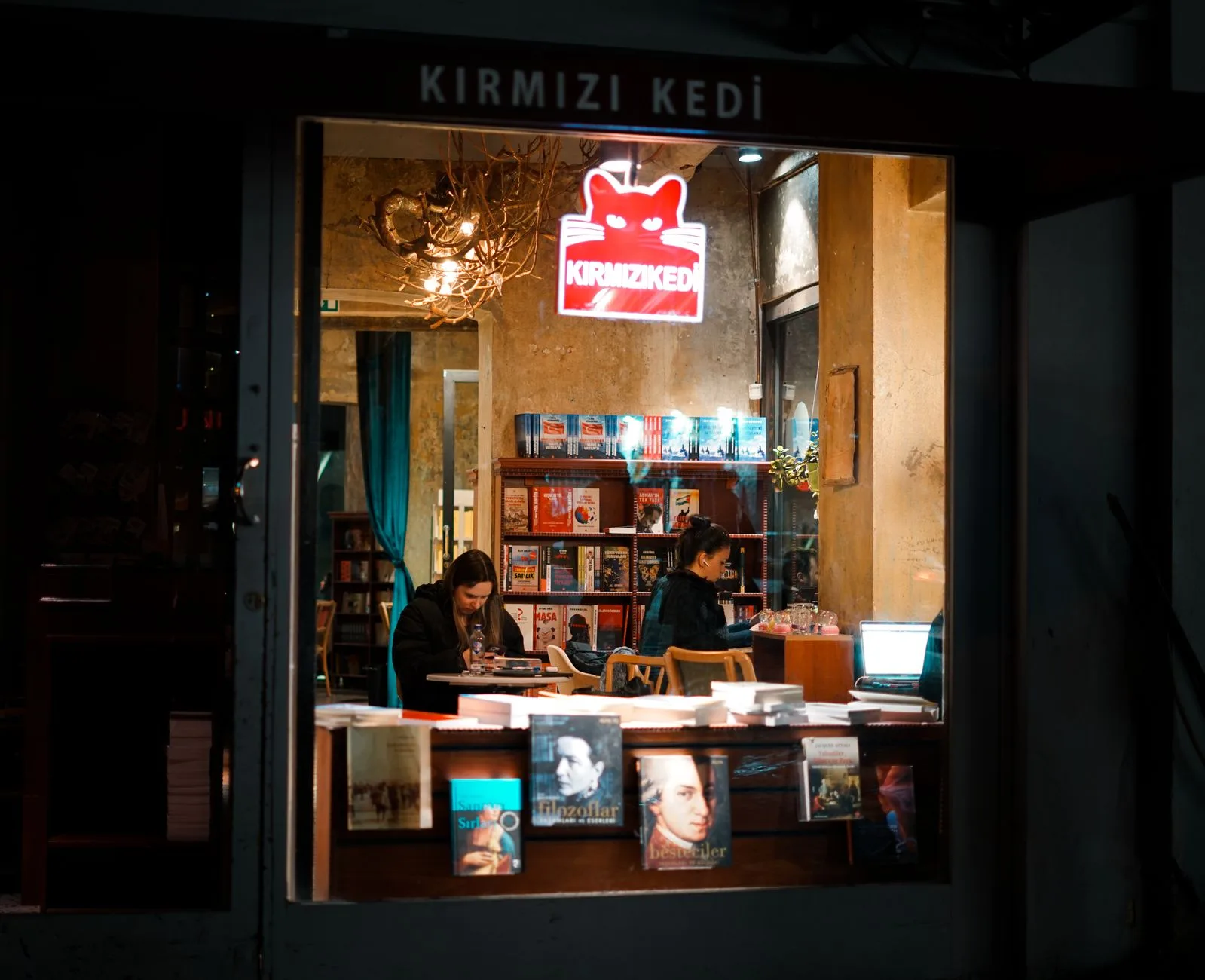 Warm and inviting view through a bookstore window at night with people reading.