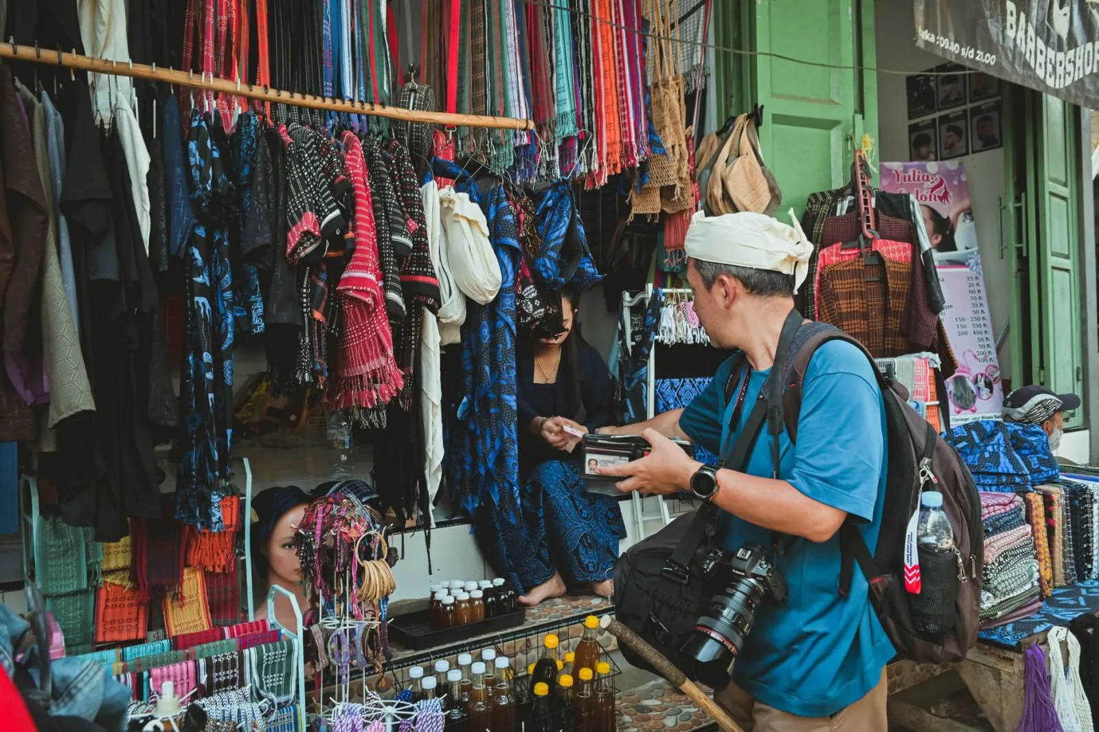 A tourist engages in a transaction at a colorful street market stall displaying traditional textiles.