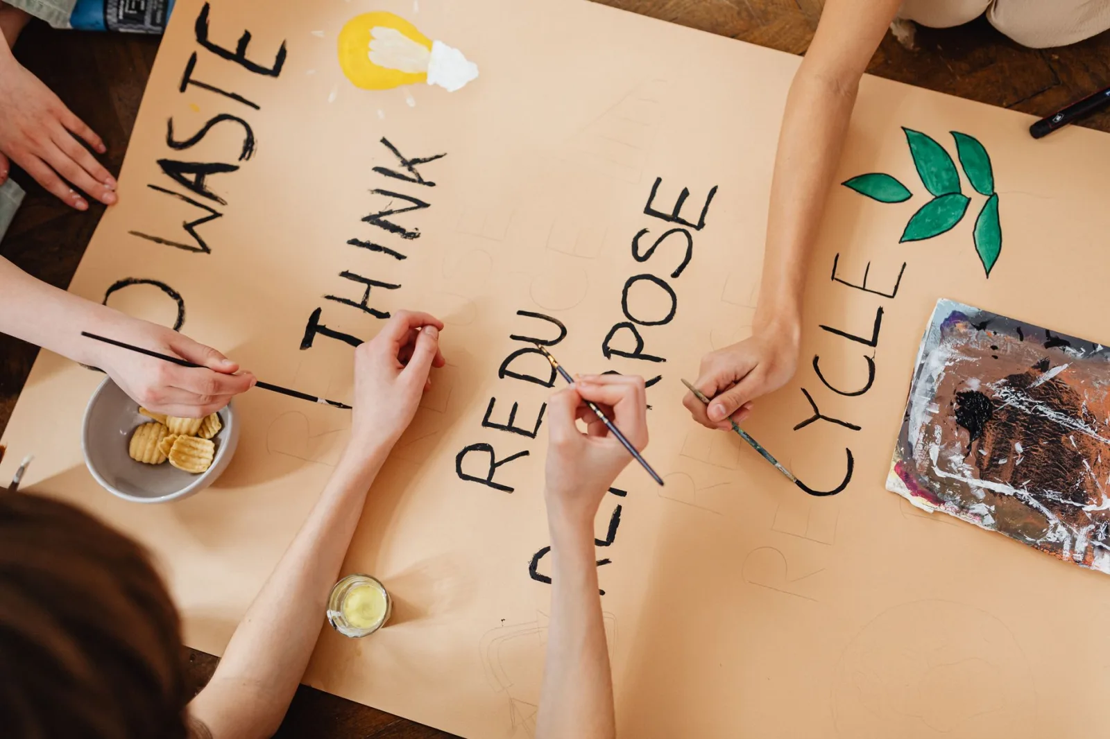 Group creating a poster on environmental themes with words like recycle, reuse, and reduce.