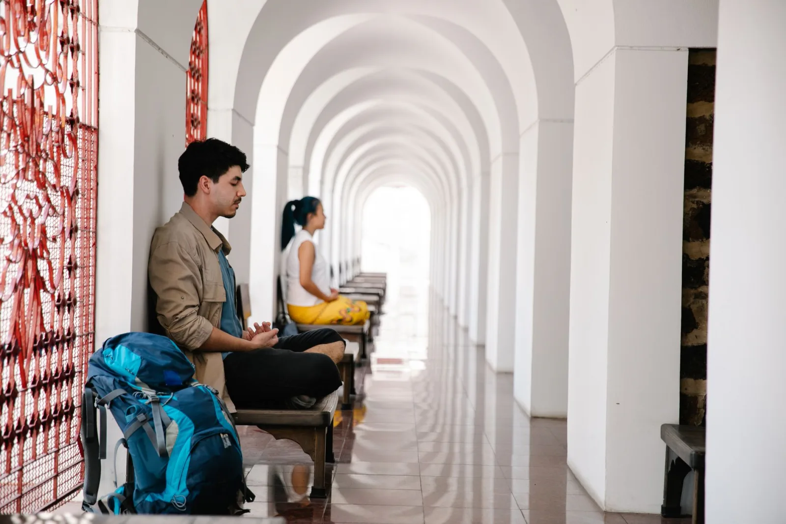 Two travelers meditate peacefully in an arched corridor, reflecting serenity and tranquility.