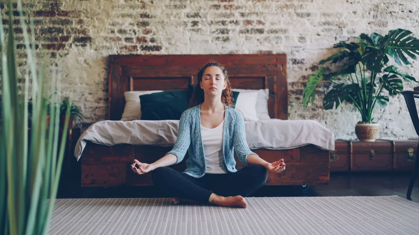 Tranquil scene of a woman meditating in a stylish bedroom with natural decor.