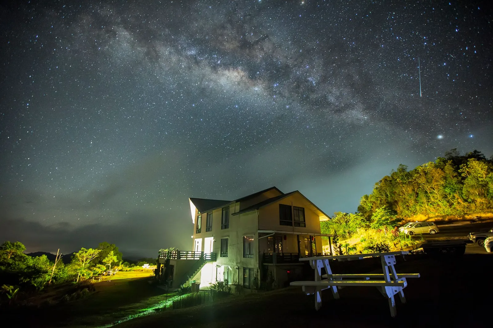 A serene countryside house under a starry night sky with the Milky Way visible.
