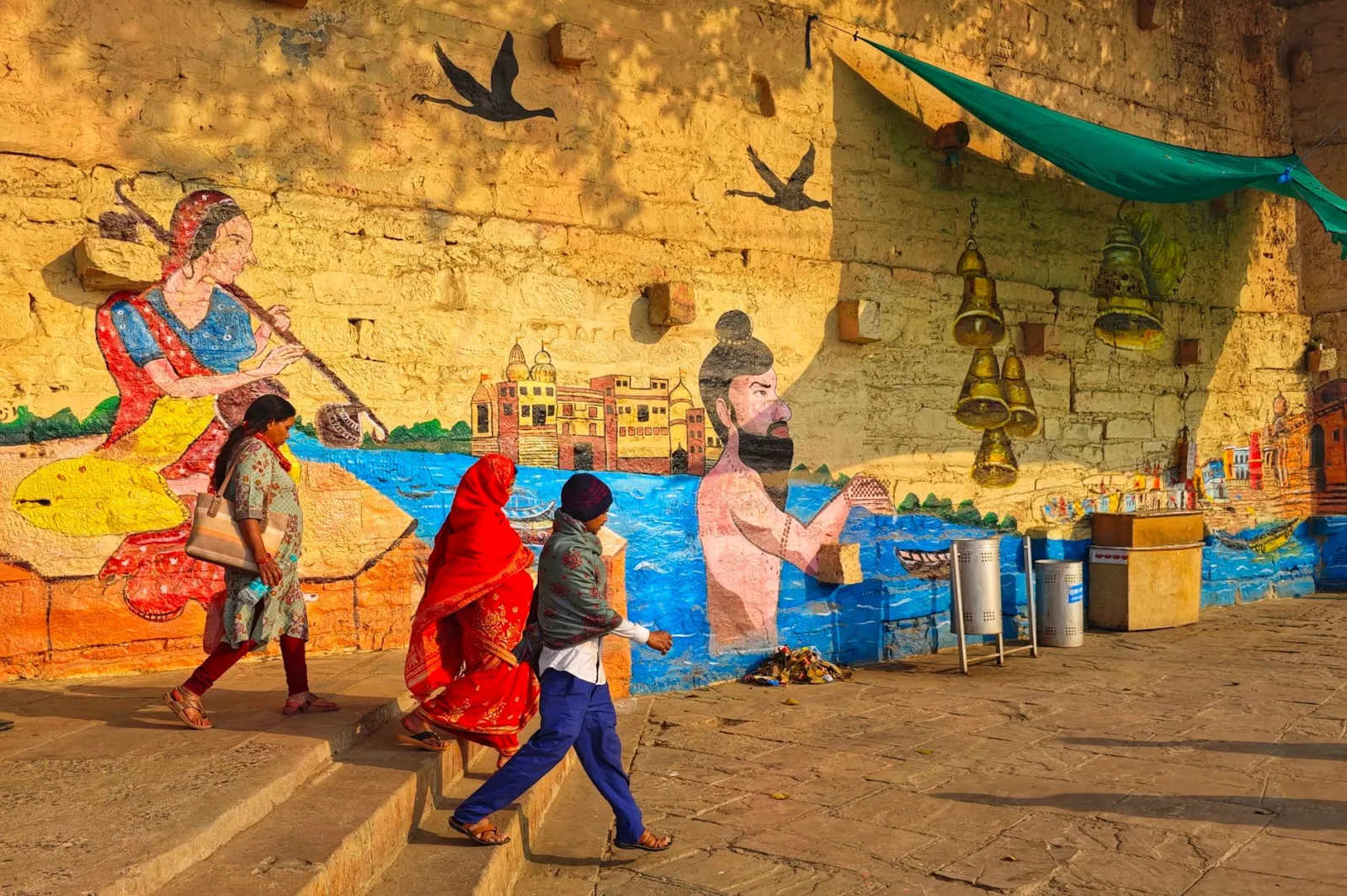 Colorful street art on a Varanasi wall with people passing by in traditional attire.