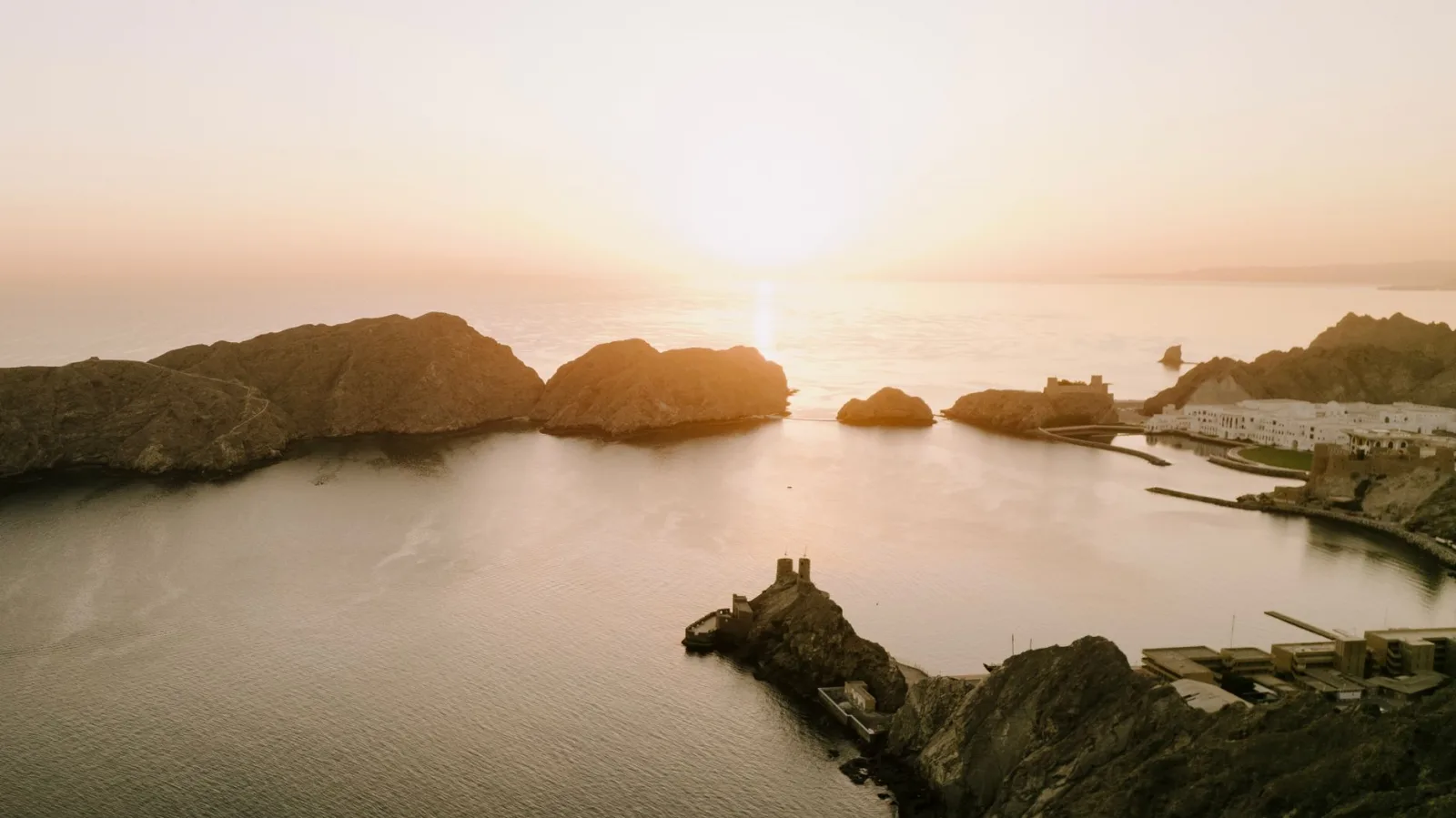 Beautiful aerial view of Oman's rocky coastline and serene sea during a golden sunset, enhancing the natural beauty of Muscat.