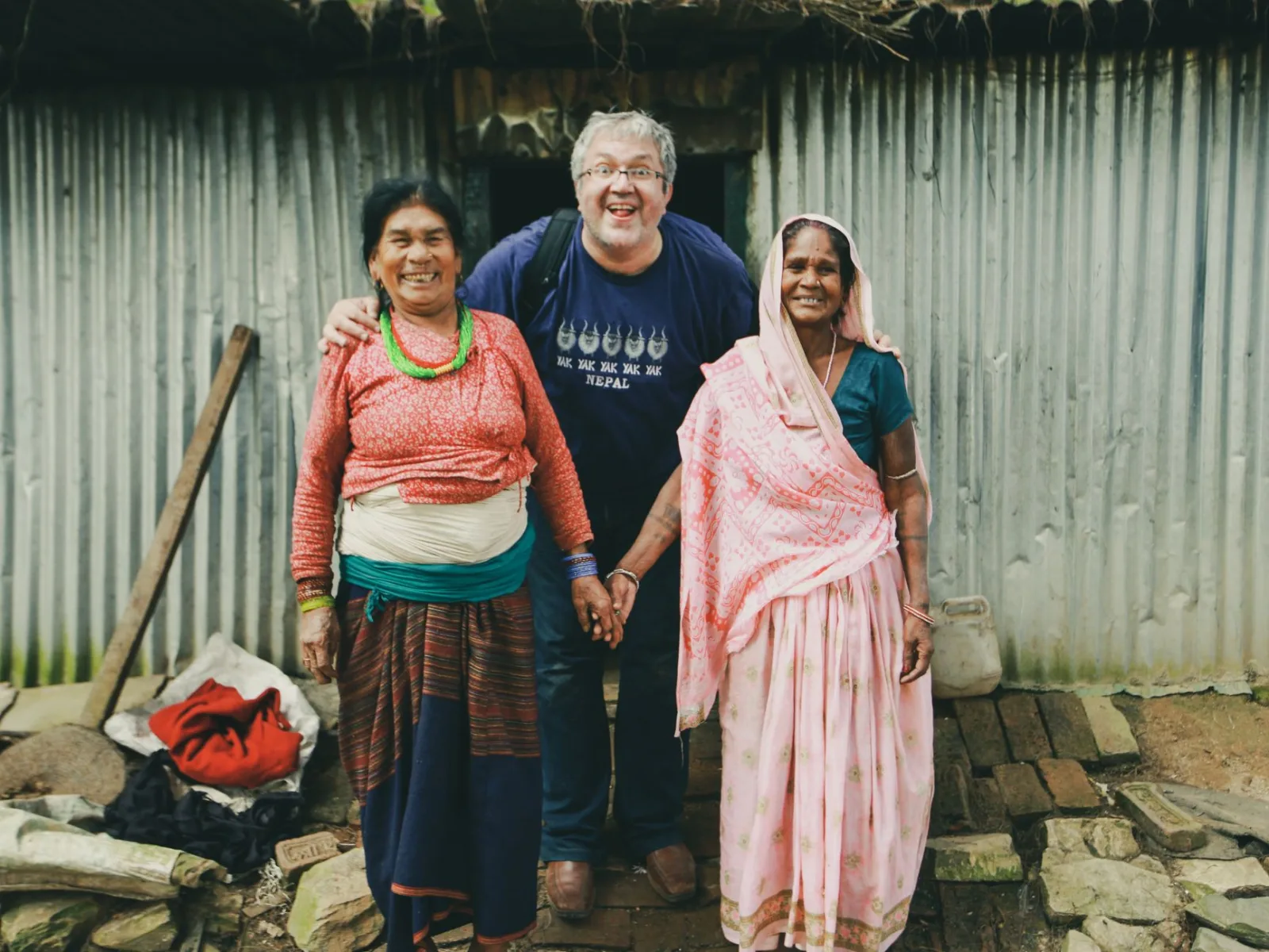 A joyful group portrait of diverse individuals standing and smiling outdoors in a rural setting.