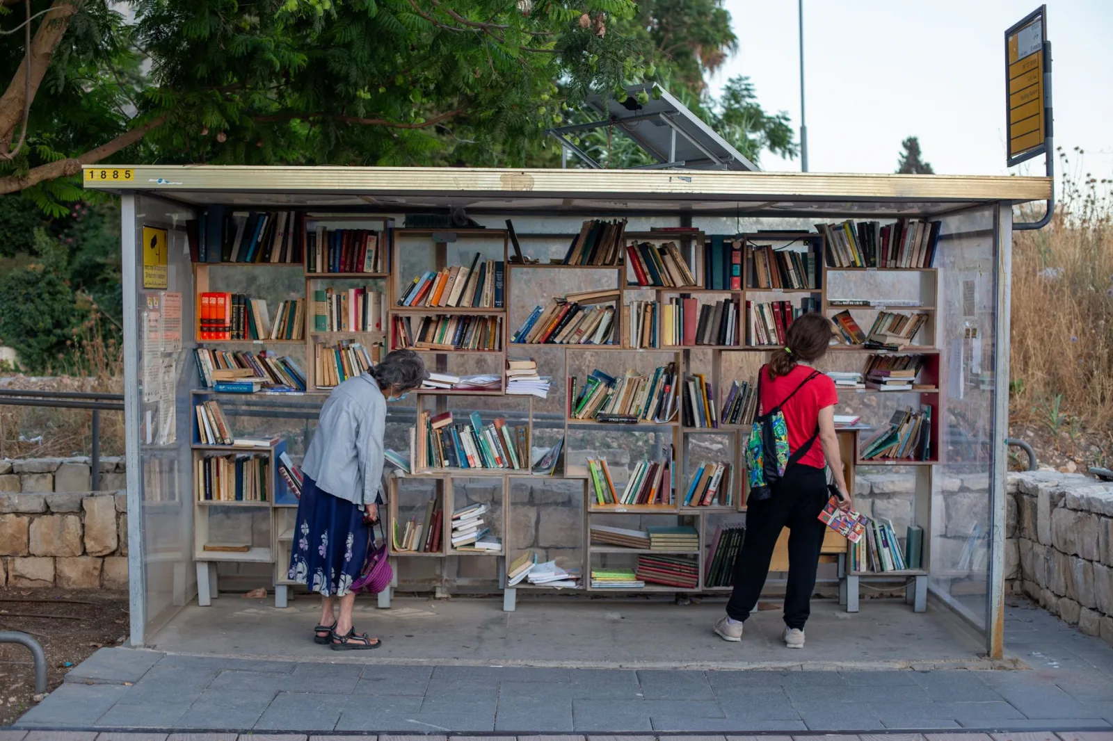 A creative bus stop transformed into a public library with two women browsing.