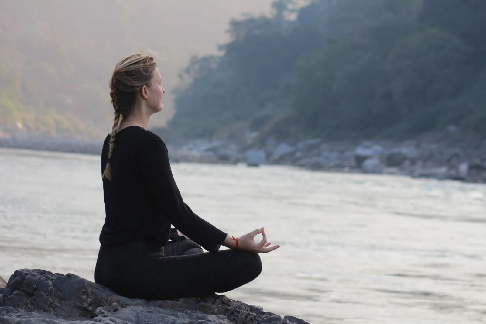 Peaceful scene of a woman meditating by the Ganges River in Rishikesh, India at sunrise.
