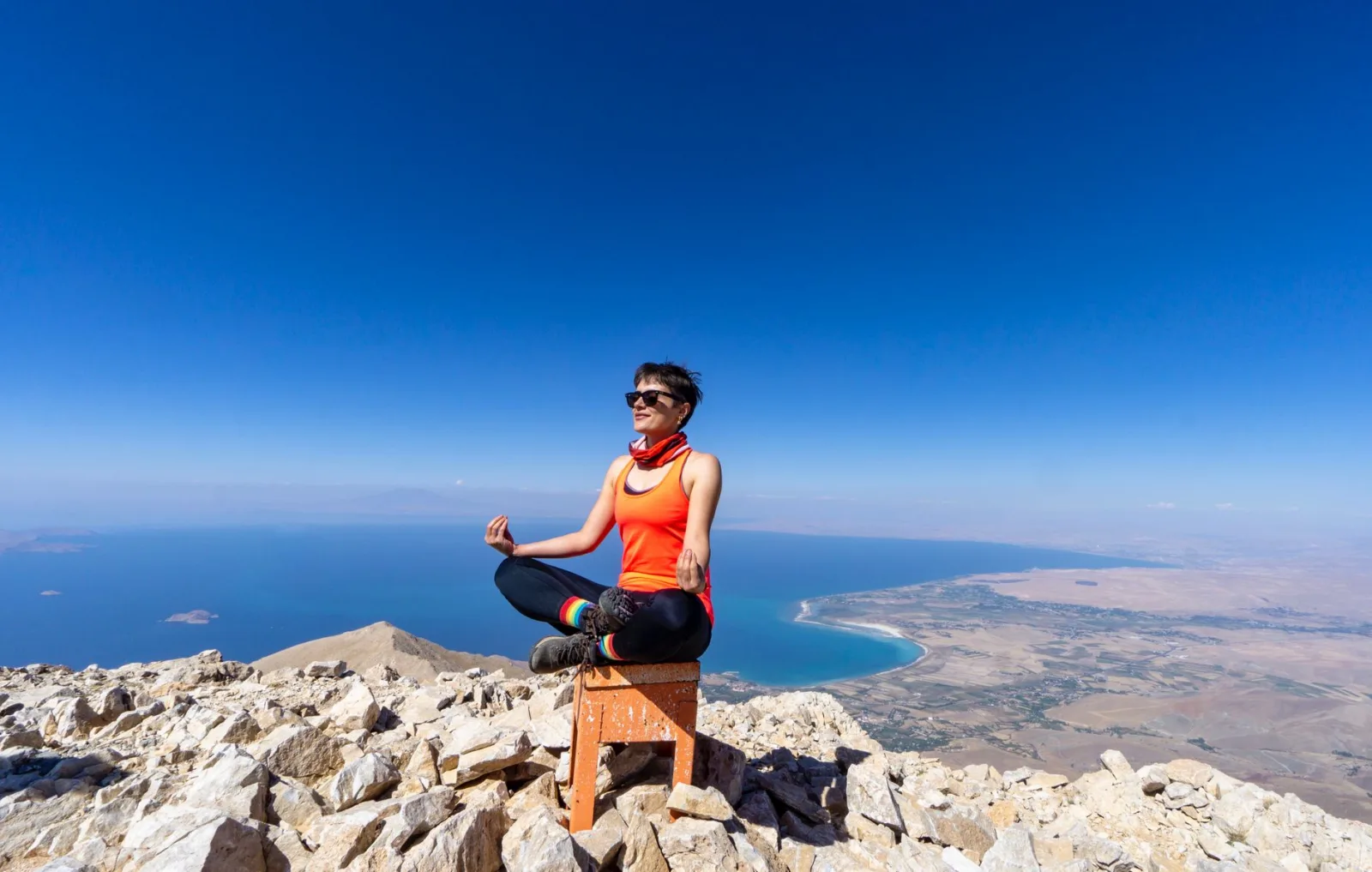 A woman practices yoga on a rocky mountain top with a clear view of the lake below, emphasizing peace and nature.
