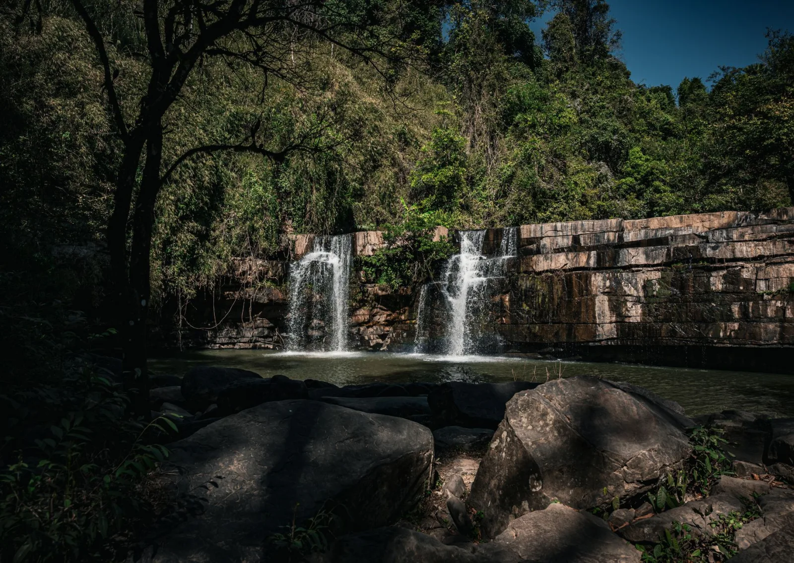 Tranquil twin waterfalls cascade into a lush Thai forest, offering a nature escape.