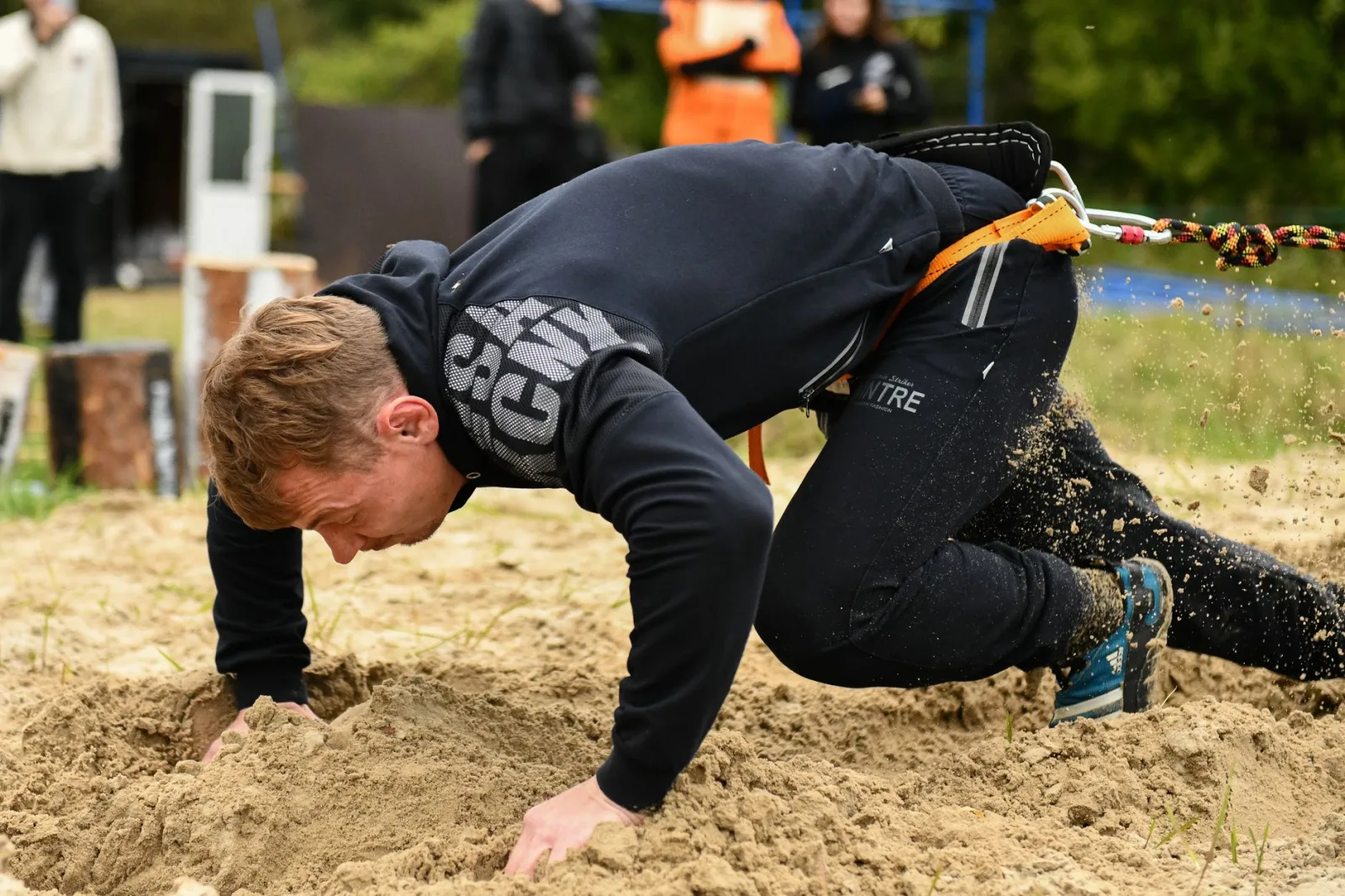 A determined man crawls through sand pulling a rope outdoors, showcasing strength and endurance.