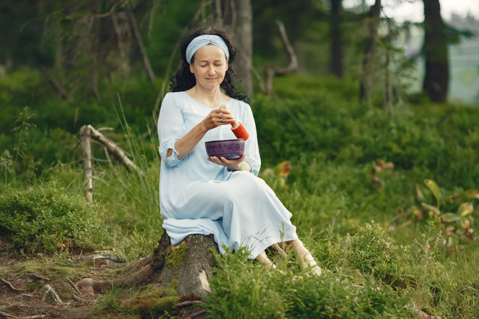A woman practicing mindfulness with a singing bowl in a serene forest setting, embracing relaxation.