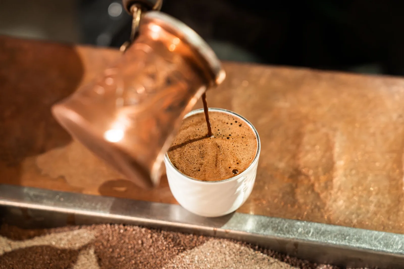 Close-up of Arabic coffee being poured from a brass dallah into a cup.