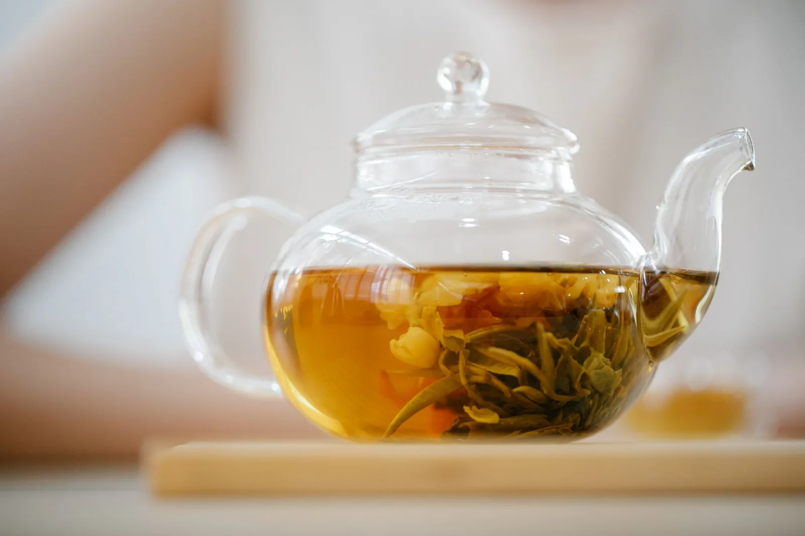A clear glass teapot containing a brewed herbal tea blend placed on a wooden surface indoors.