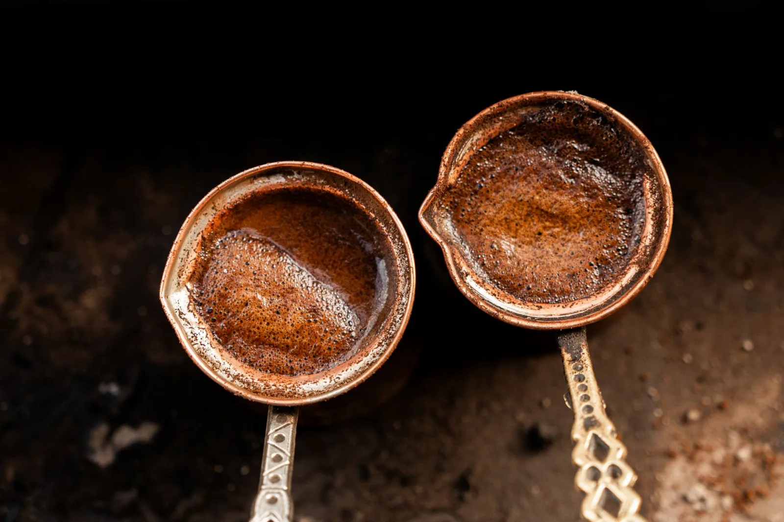 Close-up of two copper pots brewing strong Turkish coffee over hot sand.
