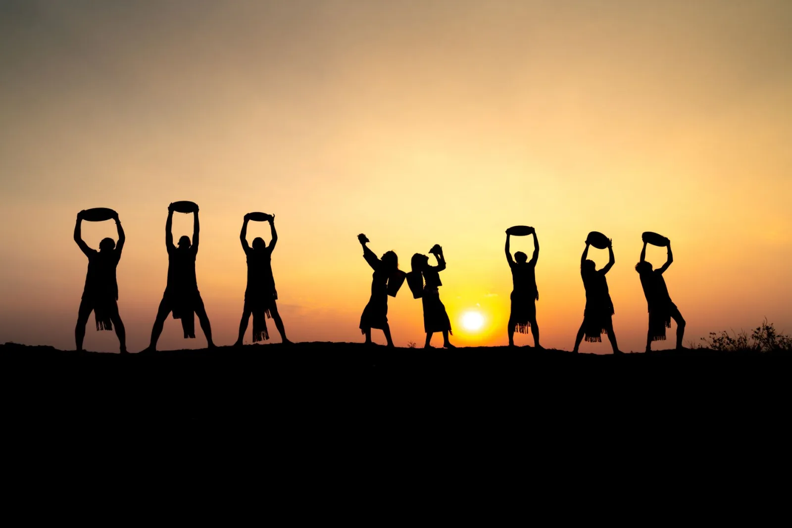 Silhouette of seven people performing traditional dance against a stunning sunset backdrop.
