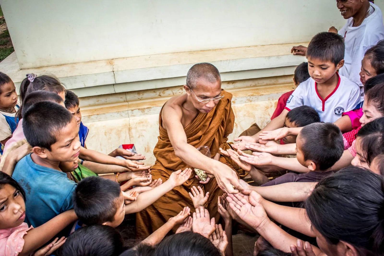 A monk shares offerings with a group of children outdoors, promoting compassion and connection.
