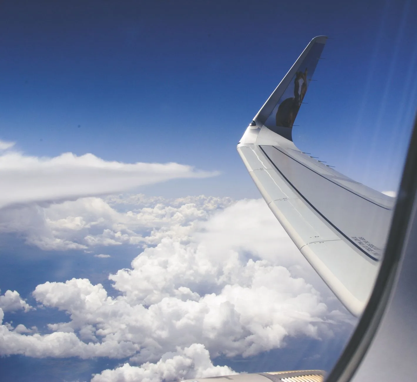 View from airplane window showcasing a wing above fluffy clouds during daylight.