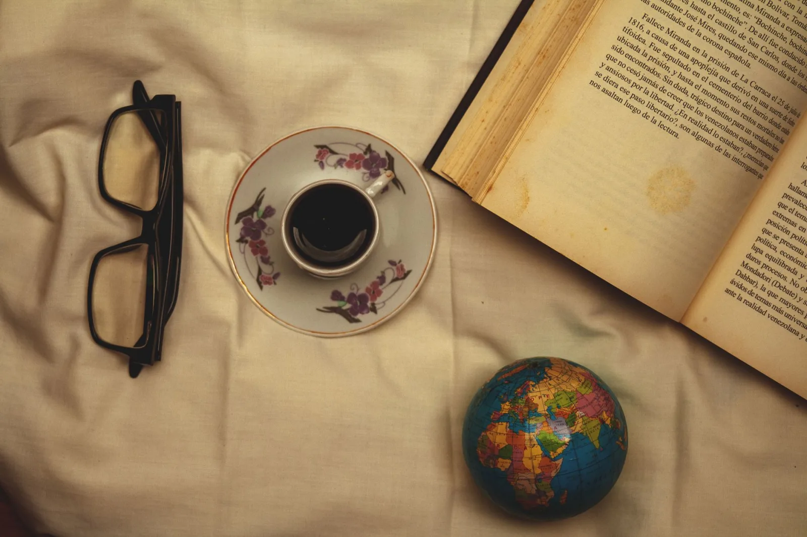 Relaxing overhead view of coffee, book, and globe on a cloth background.
