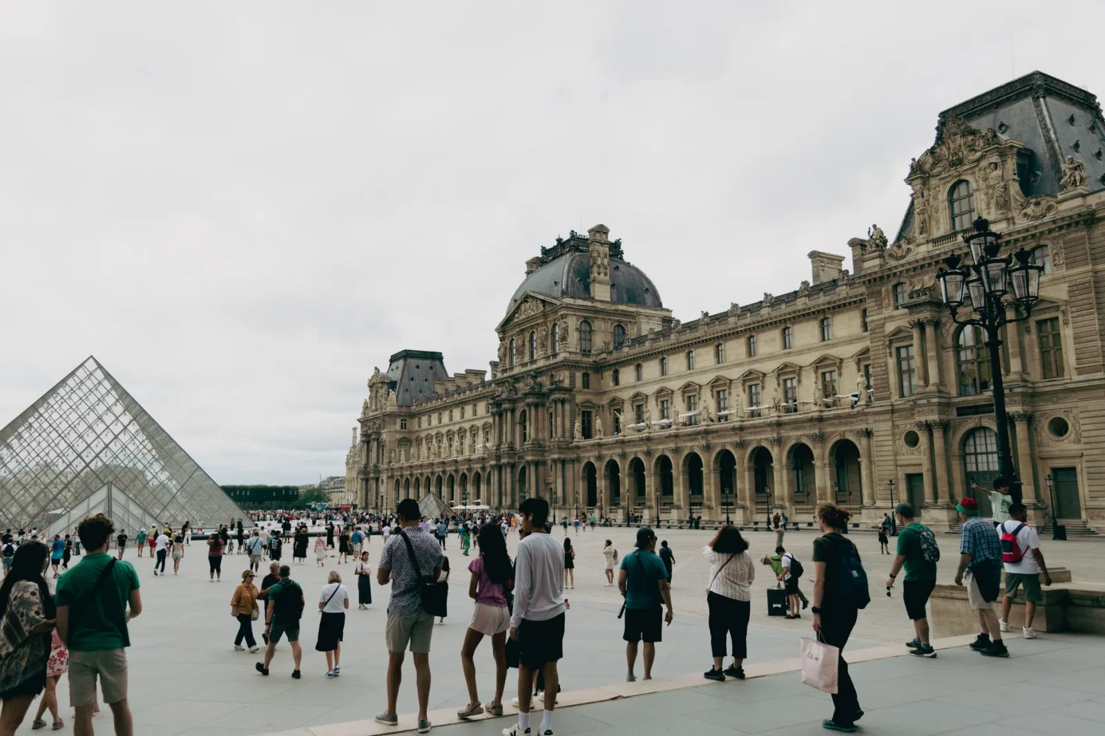 Visitors gather at the Louvre Museum in Paris with the iconic glass pyramid in view.