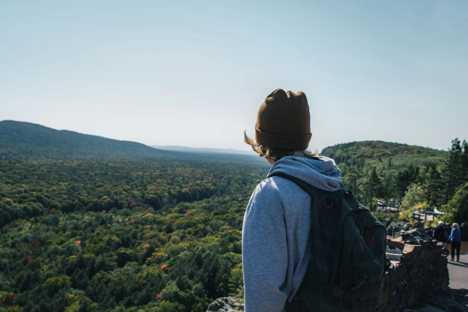 A person in a beanie and hoodie enjoys a vast mountain landscape, embodying adventure.