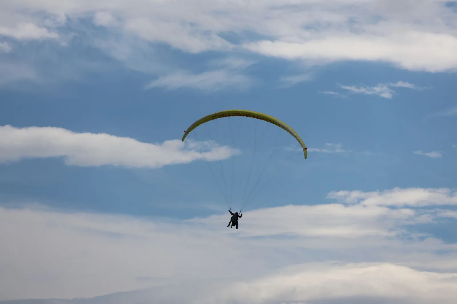 A paraglider gracefully soaring under a blue sky with scattered clouds.