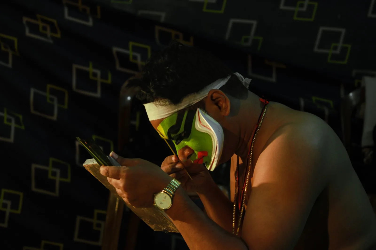 Kathakali artist applying makeup backstage in Wayanad, India for a traditional performance.