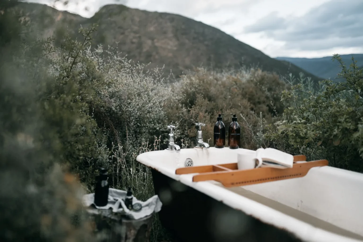 A vintage outdoor bathtub with bath essentials set in a lush natural environment.