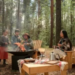 A family enjoying a camping trip with a fire pit in forest surroundings.