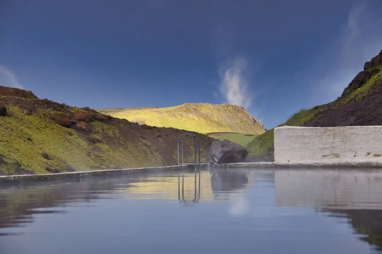 Relaxing hot spring pool in the scenic Icelandic mountains with clear blue skies.