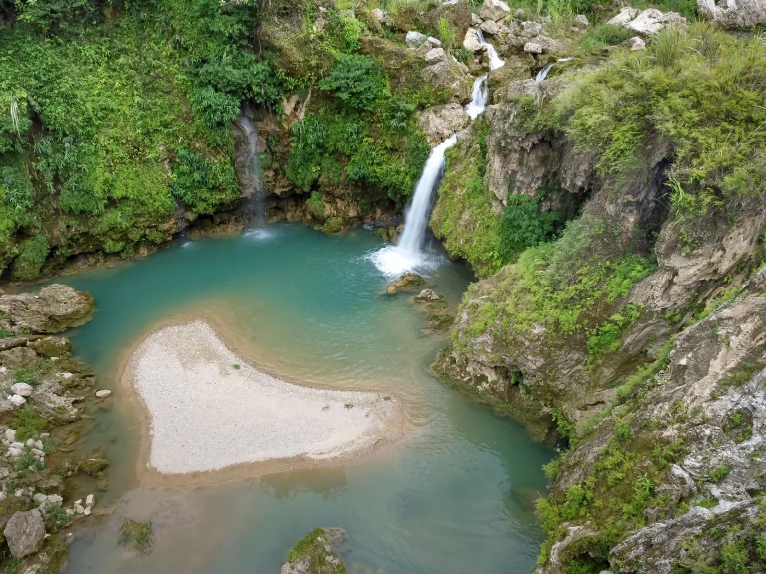 Aerial view of a serene waterfall cascading into a turquoise lagoon surrounded by greenery.