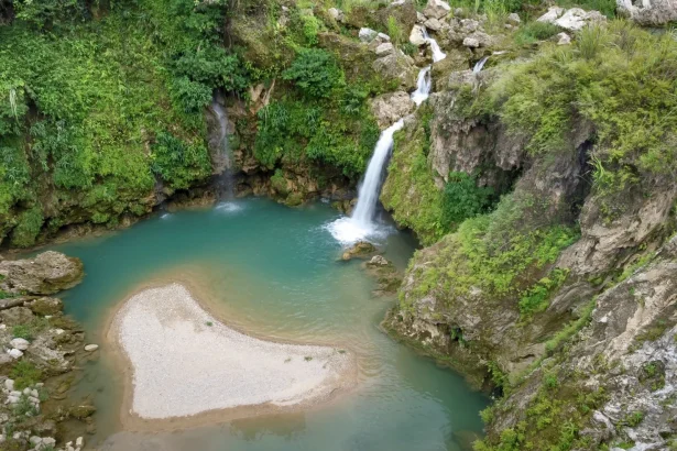 Aerial view of a serene waterfall cascading into a turquoise lagoon surrounded by greenery.