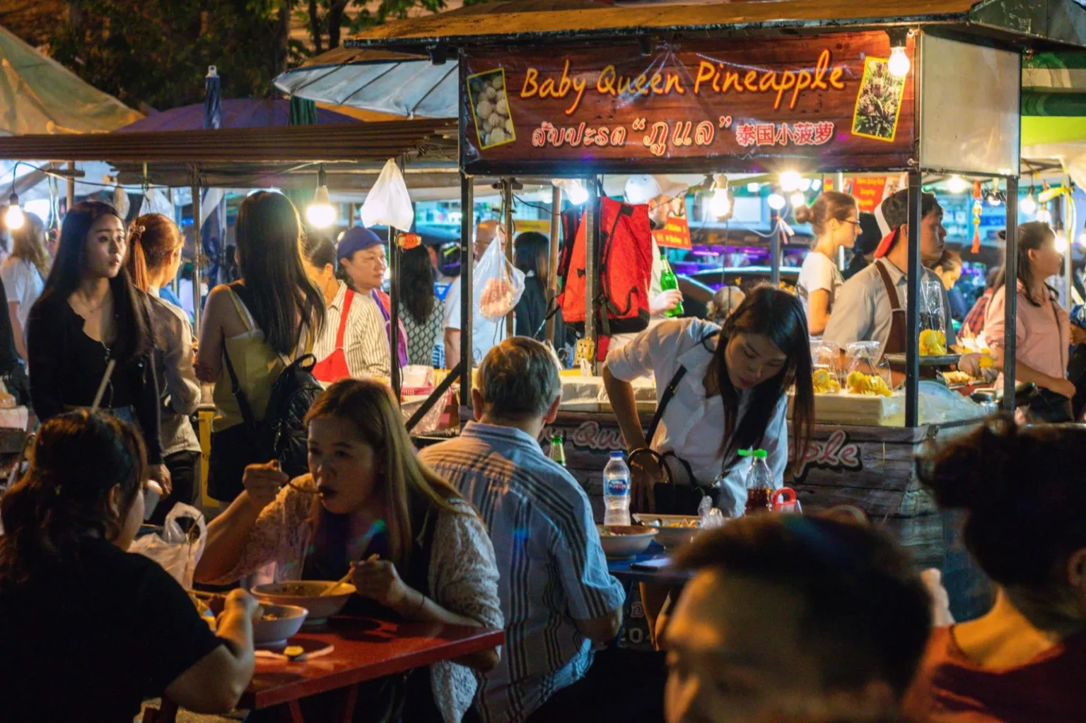 Vibrant night market with busy food stalls and diverse crowd enjoying street food.