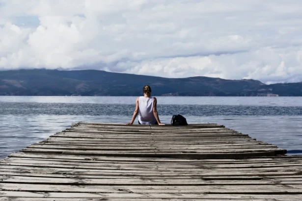 Woman sitting on a wooden pier, enjoying the serene lake view and mountains.