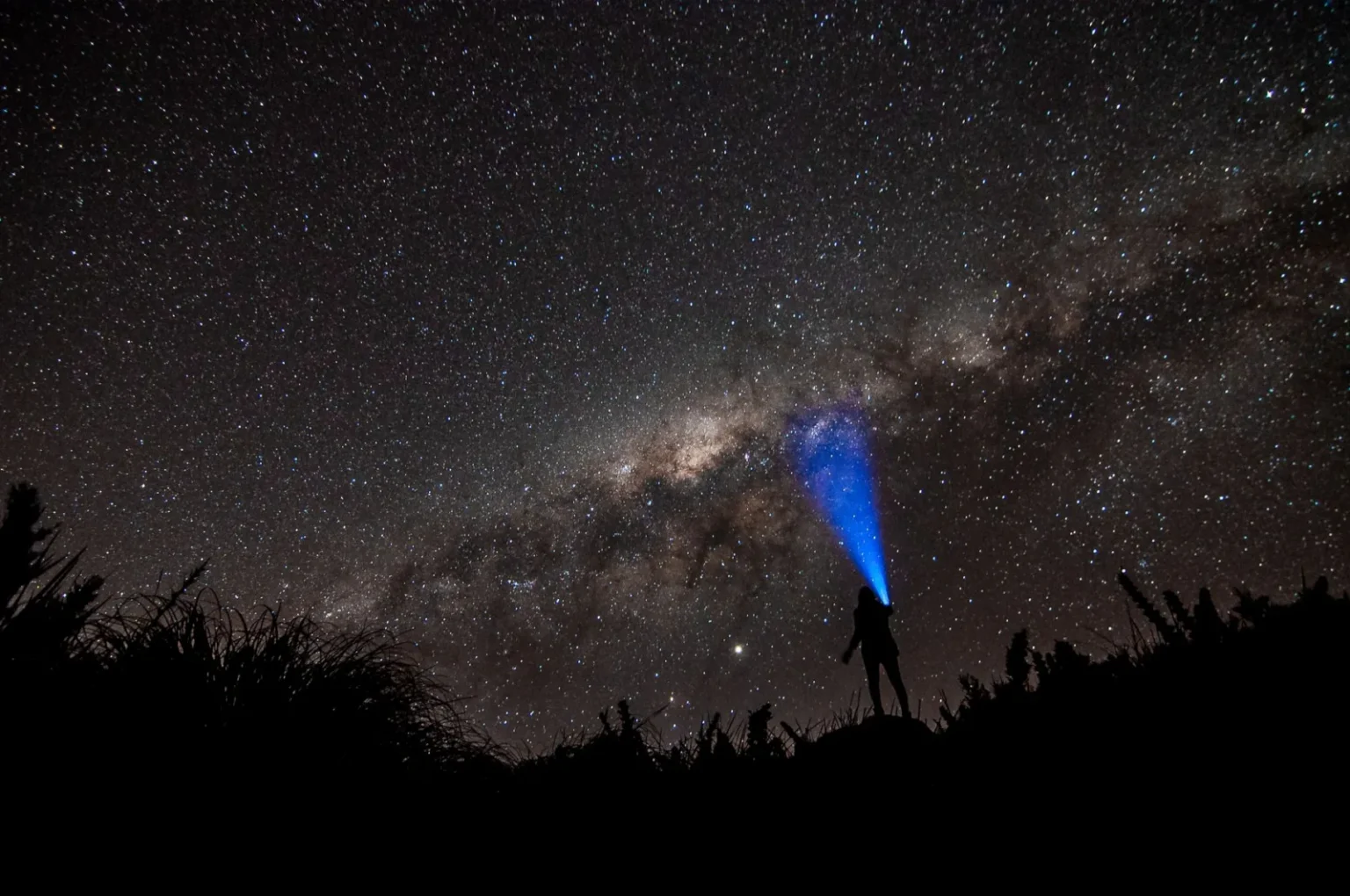 Person with flashlight under the starlit sky of the Milky Way galaxy at night.