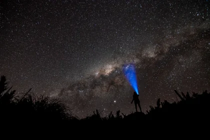 Person with flashlight under the starlit sky of the Milky Way galaxy at night.