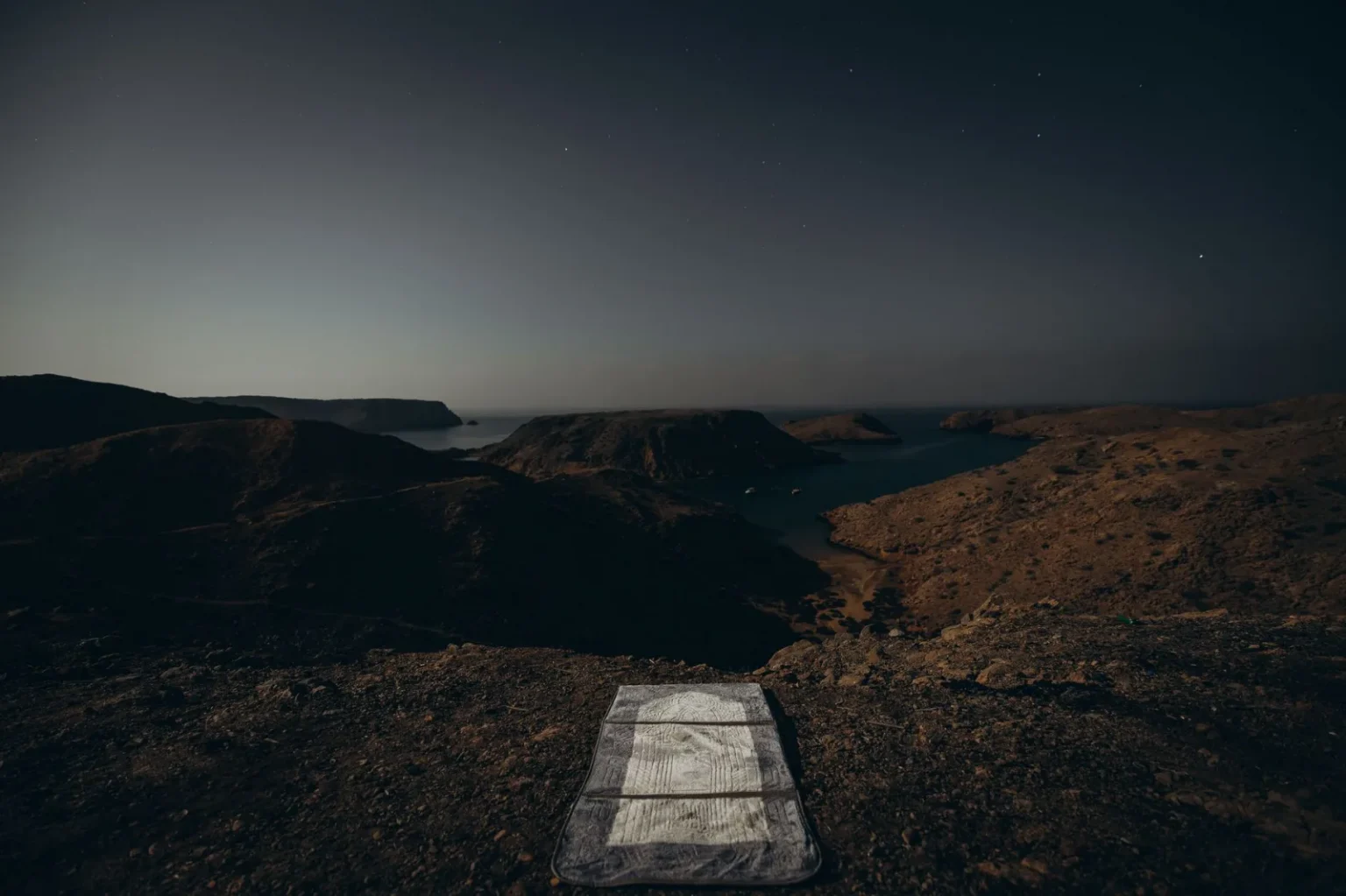 A tranquil night view of rocky landscapes and starry skies near the coast in Muscat, Oman.