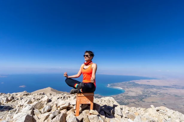A woman practices yoga on a rocky mountain top with a clear view of the lake below, emphasizing peace and nature.