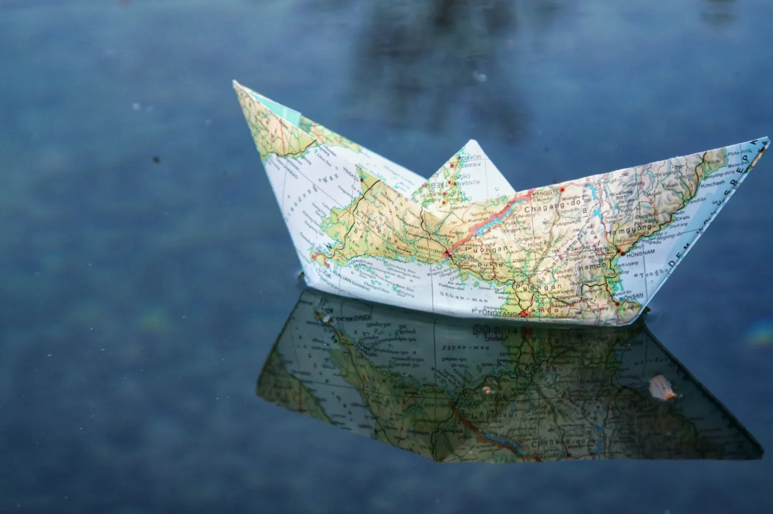 A paper boat folded from a map floats on water, creating a unique reflection.