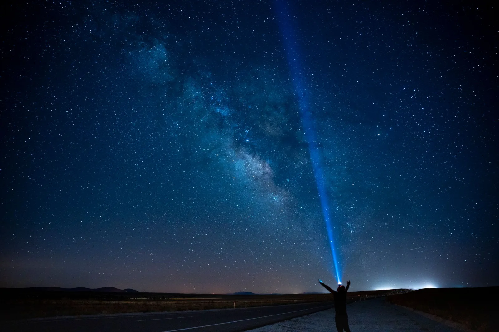 A person stands on a road under the Milky Way, pointing a beam of light into the starry night sky in Karaman, Türkiye.