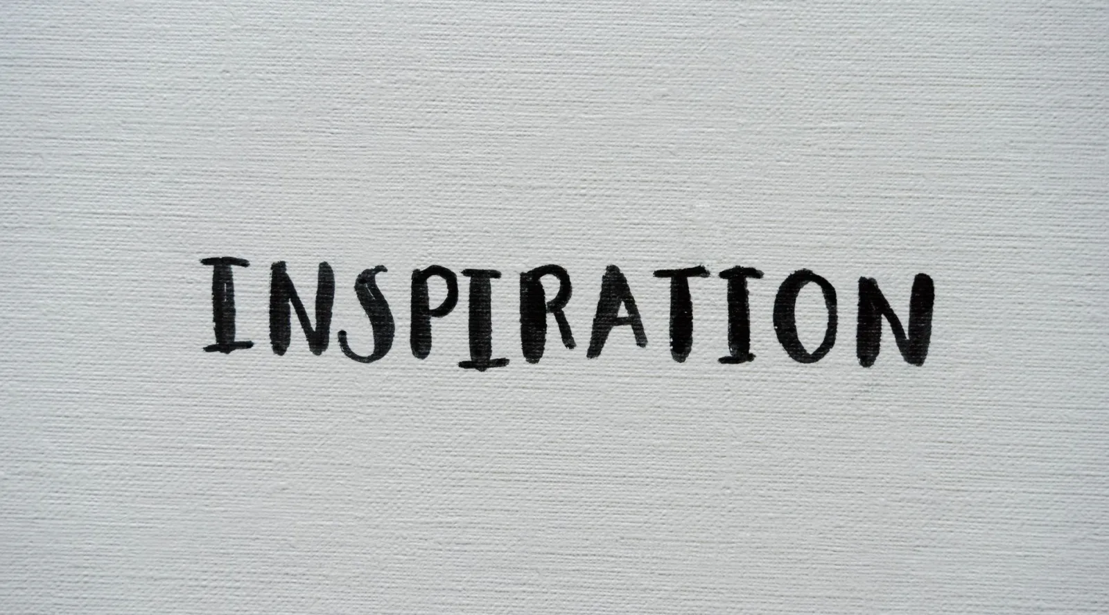 Simple and artistic black 'Inspiration' text on white canvas background.