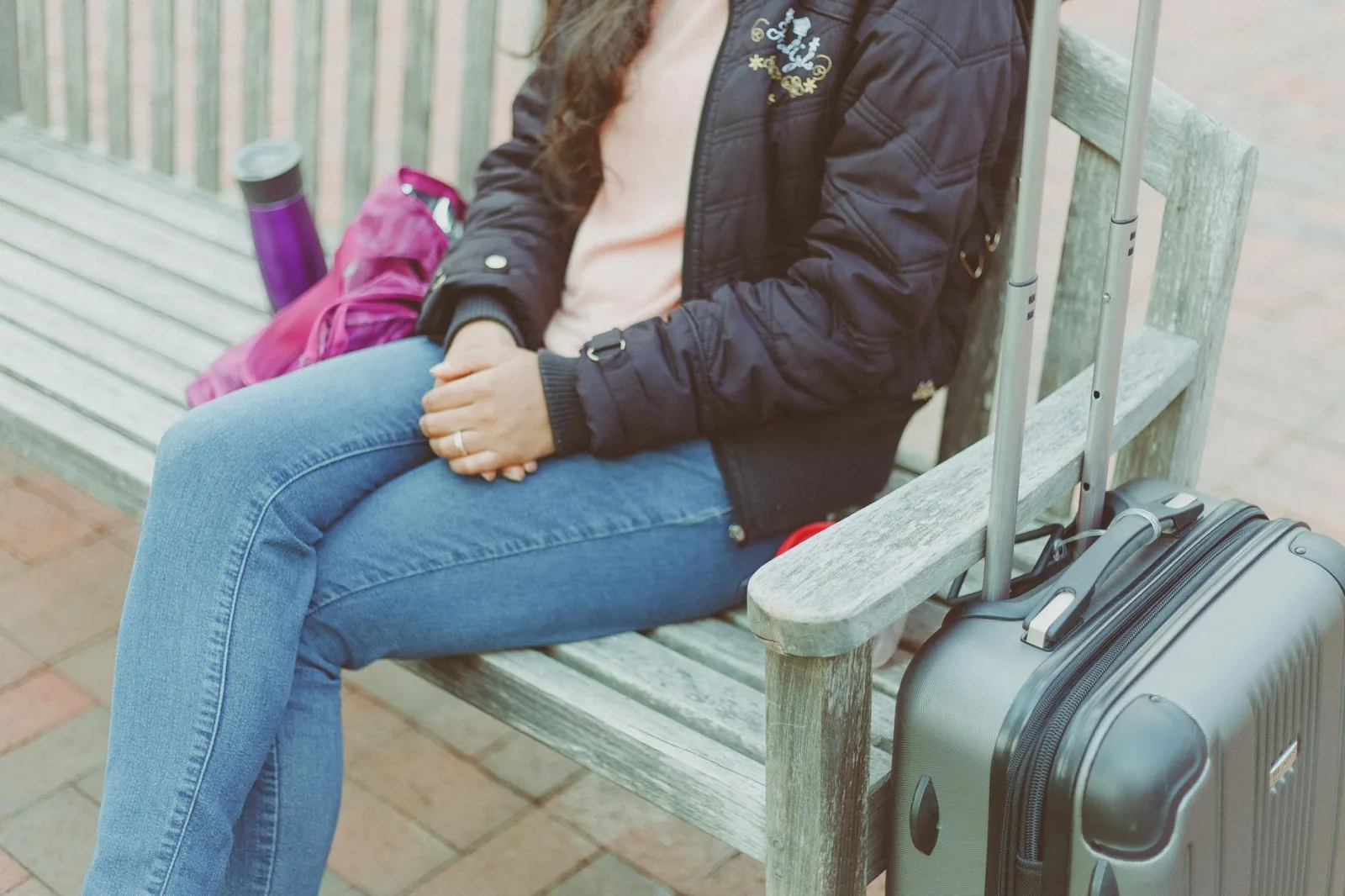Casual woman sitting on bench with luggage in Columbia, MD.