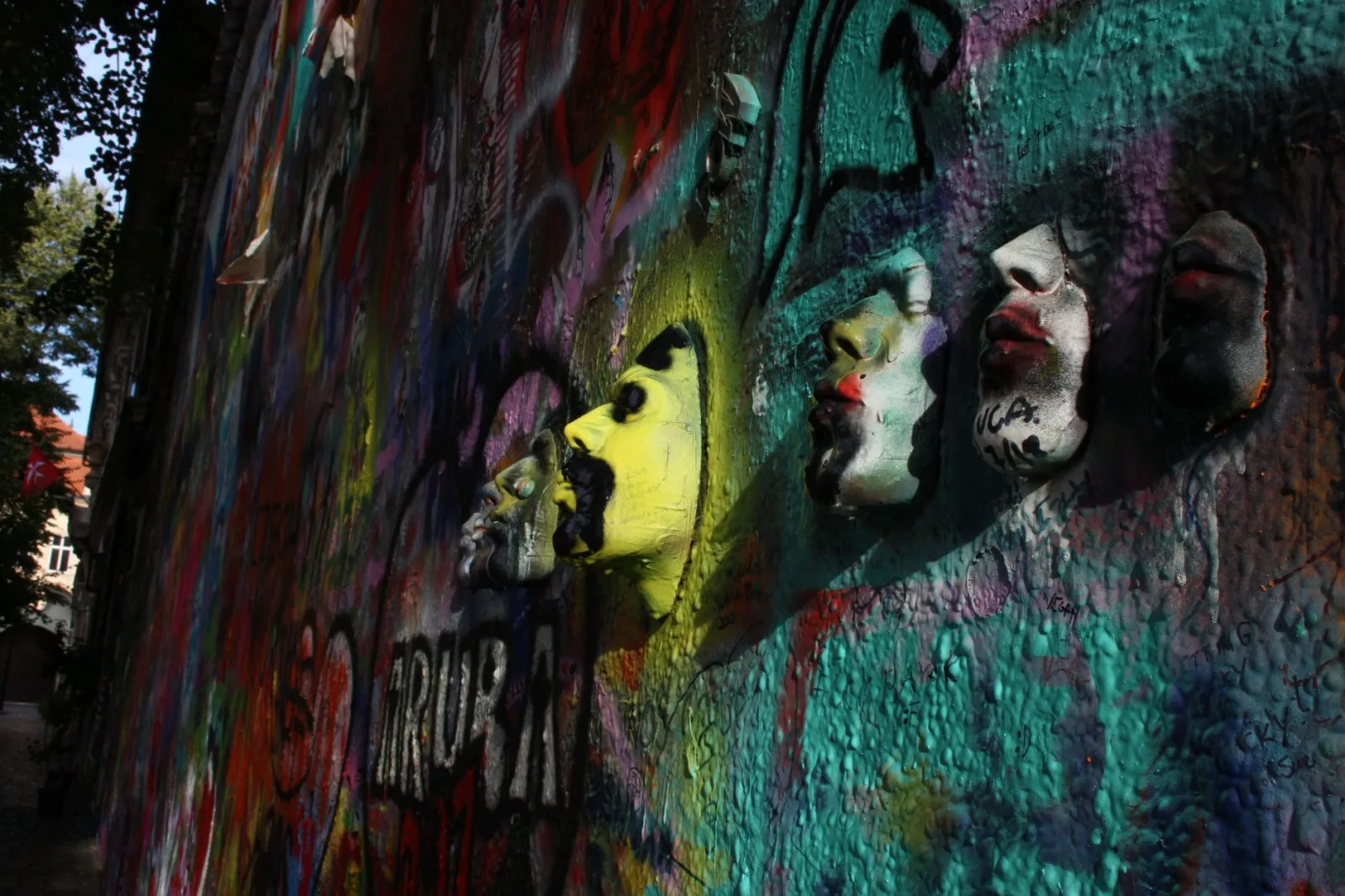 Dynamic street art featuring colorful graffiti and 3D masks on a textured wall.