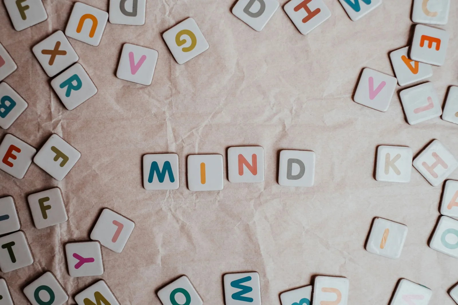 Close-up of scattered letter tiles spelling 'mind' on crumbled paper background.