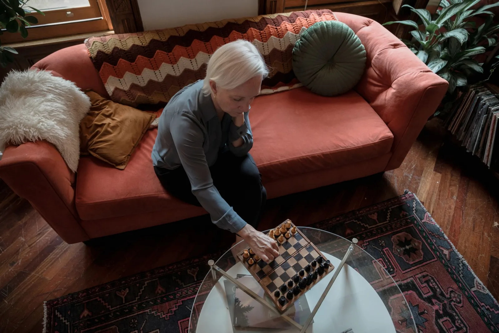 Elderly woman playing chess alone on the couch at home, creating a quiet and contemplative atmosphere.