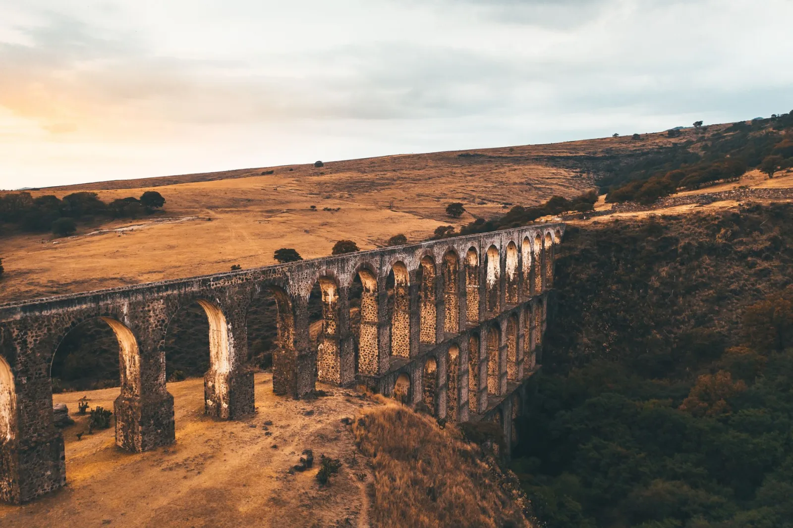 A magnificent stone aqueduct stretches through a serene valley under a warm sunset sky.