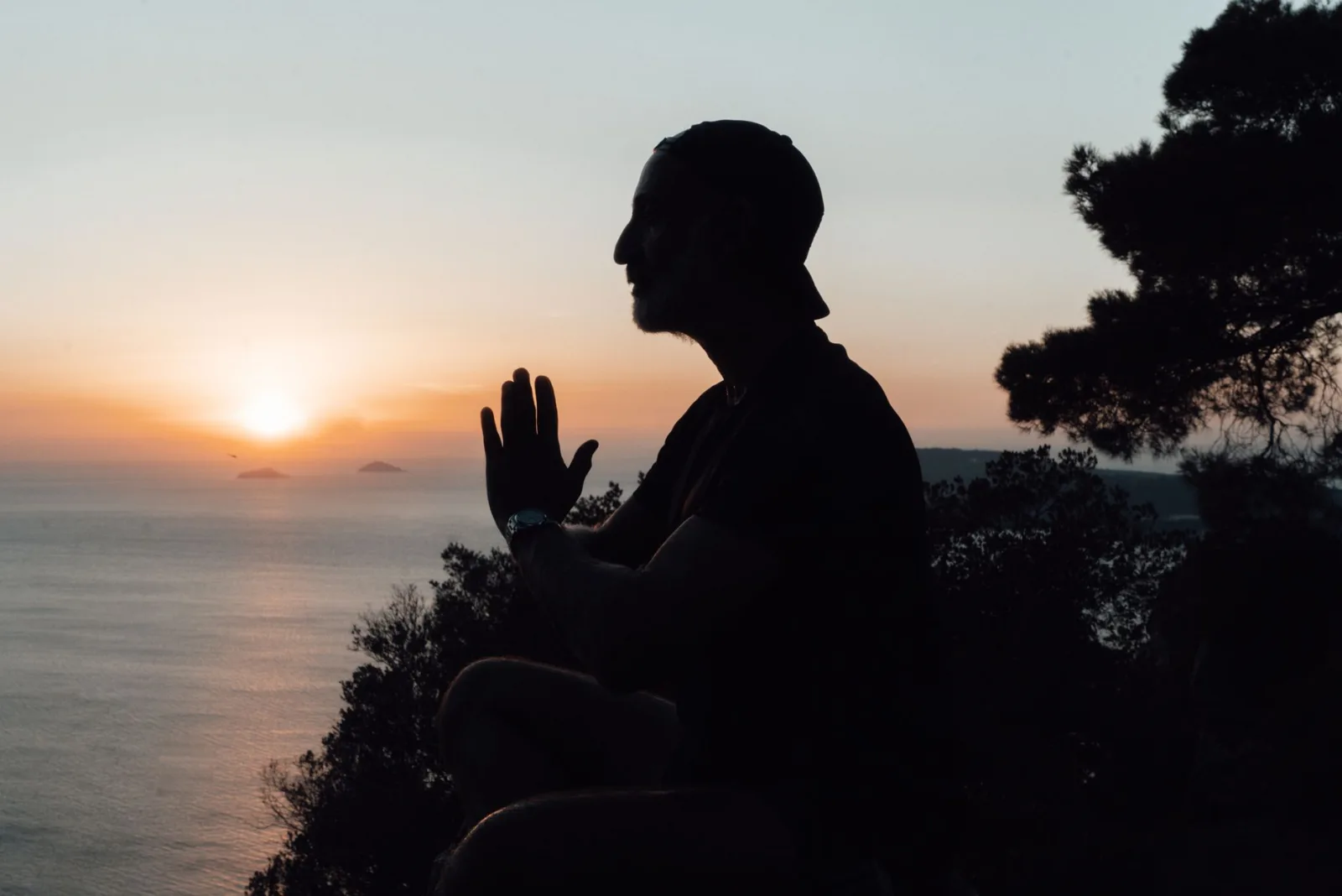 Side view silhouette of serene male sitting in lotus pose and meditating on peaceful seacoast during scenic tranquil sunset