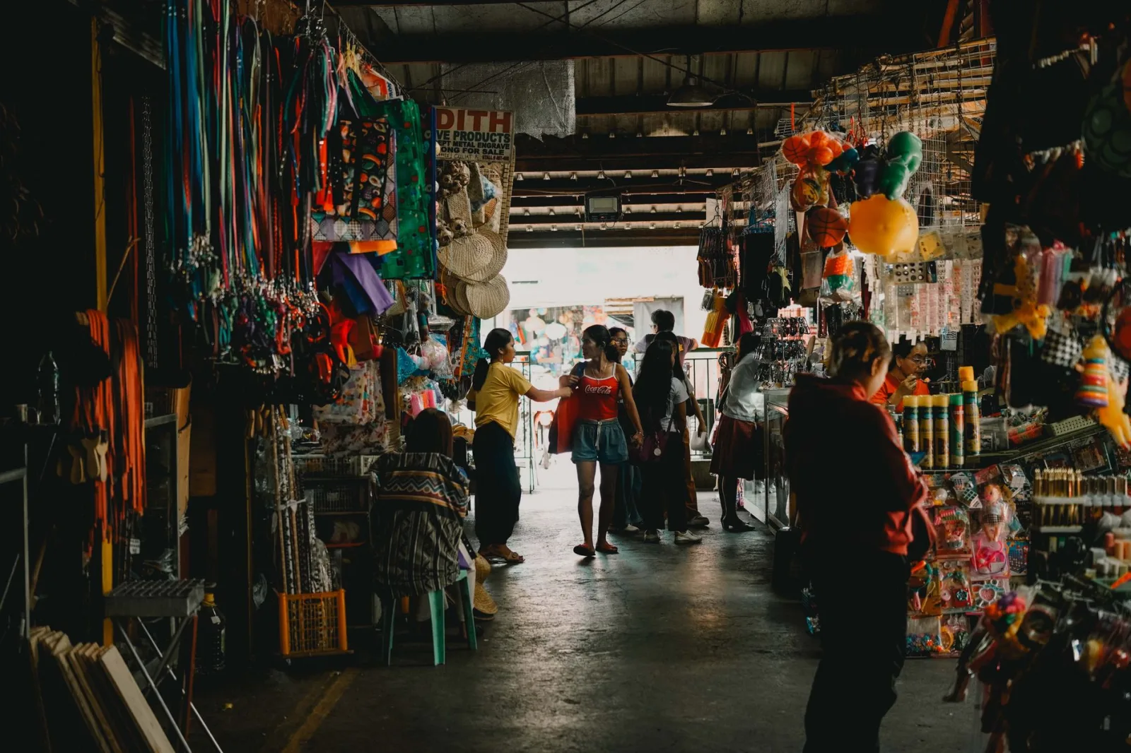 Vibrant indoor market scene with shoppers exploring diverse stalls filled with colorful merchandise.